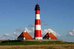 a red and white lighthouse sitting on top of a field at Gaestehaus-Meene-Menten-Wohnung-MM-2 in Süderhöft