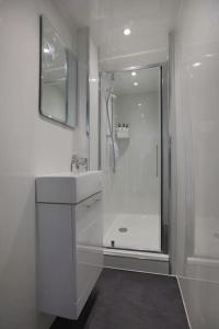 a white bathroom with a shower and a sink at Cosy & Central Broughton 2BR Apt near City Centre in Edinburgh