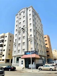 Relax Inn Furnished Apartments Hawally في الكويت: مبنى ابيض كبير فيه سيارات تقف امامه