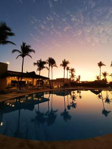 a pool with palm trees in front of a sunset at Hotel Tres Vidas Acapulco in Barra Vieja