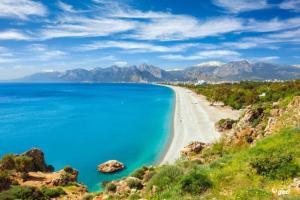 a beach with blue water and mountains in the background at Antalya’nın nezih semtinde daire in Antalya