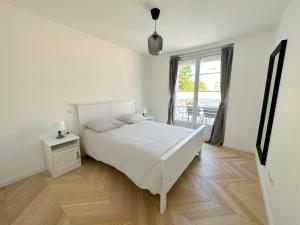 a white bedroom with a bed and a window at Les appartements du Carnot - Terrasses et Jardins in La Rochelle