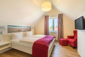 a bedroom with a large bed and a red chair at Hotel Deichkrone - Familotel Nordsee in Norddeich