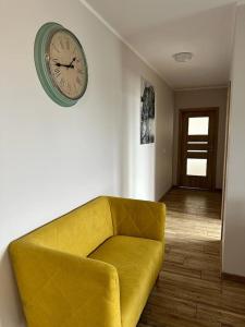 a yellow couch in a room with a clock on the wall at Apartamenty Firfas Rodzinny 11 in Bydgoszcz