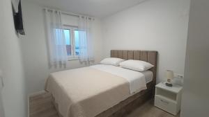 a white bedroom with a bed and two windows at Apartmani Srdarović in Drage