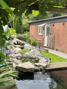 a garden with a pond with rocks and a house at Patio lodge with forest access close to beaches in South Wootton