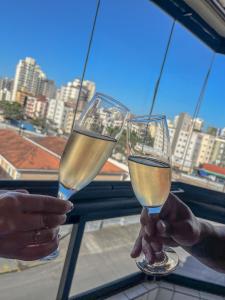 2 personnes tenant des verres de vin blanc dans l'établissement Apartamento com Varanda e Suíte Enseada Guarujá, à Guarujá