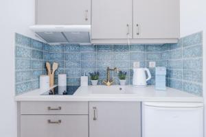 a kitchen with white cabinets and blue tiles at RODAVGI APARTMENTS in Andros