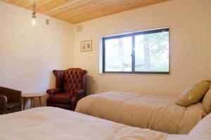 1 dormitorio con 2 camas, silla y ventana en 1日1組様限定 黒姫山の絶景を楽しむ貸切サウナ付き一軒家, en Shinano