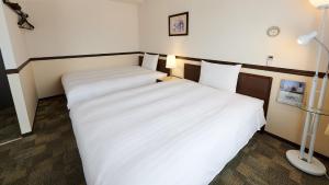 two beds in a hotel room with white sheets at Toyoko Inn Osaka Namba Nippombashi in Osaka