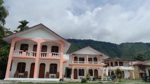 a pink and white house with mountains in the background at Hotel Barbara in Tuktuk Siadong