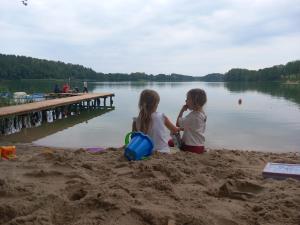 two little girls sitting in the sand near a pier at Pole namiotowe - namiot do wynajęcia - Kurka Wodna !!! in Mikołajki