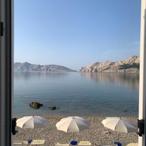 two umbrellas sitting on a beach near the water at Marija Seršić “Narca” in Baška