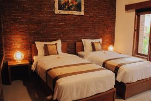 two beds in a room with a brick wall at The Govardhan Homestay in Canggu
