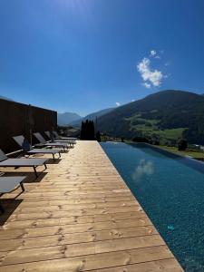a row of chaise lounges on a wooden walkway by a pool at Hotel Lahnerhof in Vipiteno