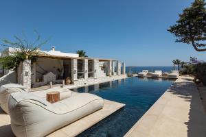 a pool with couches and chairs next to a house at Amalgam Homes Paros Beachfront Villa in Ambelas