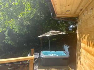 una bañera de hidromasaje bajo una sombrilla en una terraza en Unique Orchard Lodge for couples with hot tub, en Strathaven