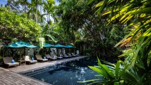 a resort pool with lounge chairs and umbrellas at Lynnaya Urban River Resort in Siem Reap