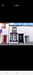 a white building with a red door on a street at The Snug in Cockermouth