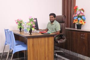 un hombre sentado en un escritorio con un ordenador en Leo Home Stay, en Tirupati