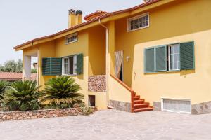 a yellow house with green shutters and stairs at Casa Antonietta in SantʼAnna Arresi