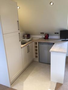 a small kitchen with white cabinets and a refrigerator at Glen House Annexe in Bourne