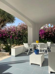 a patio with white chairs and a table and purple flowers at Archiammare Sea in San Lorenzo