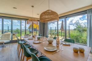 a dining room with a long table and chairs and windows at Natuurvilla 14 Westerkolk in De Waal