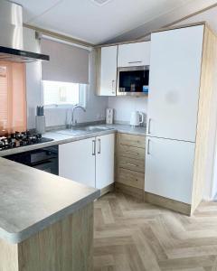 uma cozinha com armários brancos e um frigorífico branco em Hafan Y Môr Caravan - Pwllheli em Chwilog