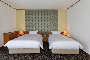 2 bedden in een hotelkamer met witte lakens bij Suikouen Hotel in Kurume