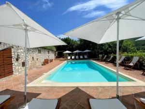 - une piscine avec deux parasols blancs et des chaises dans l'établissement Spoleto Splash Cisternasleeps 23wifiaircon - cute with beautiful garden, à Strettura