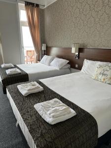 two beds in a hotel room with towels on them at Glastonbury Hotel in Eastbourne