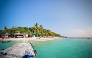 a beach with palm trees and a boat in the water at Tuna Bay Island Resort in Perhentian Islands