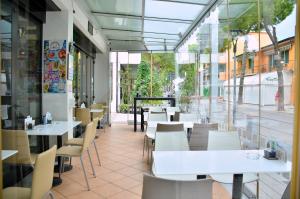 Un restaurante con mesas y sillas blancas y ventanas. en Hotel Etna, en Lignano Sabbiadoro