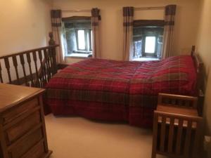 a bedroom with a bed with a red blanket and two windows at Knoll Top Cottage in Todmorden