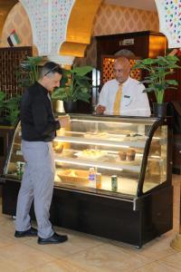 Dois homens em frente a um balcão de padaria. em Sharjah International Airport Hotel em Sharjah