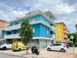 un bâtiment bleu avec des voitures garées dans un parking dans l'établissement Appartamento Stella, à Bibione