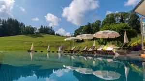 una piscina con sillas, sombrillas y una colina en Hotel Kesslermühle en Hinterzarten