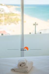 a white towel sitting on a bed in front of a window at #086 Fish House by Home Holidays in Albufeira