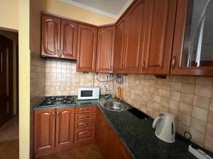 eine Küche mit Holzschränken, einer Spüle und einer Mikrowelle in der Unterkunft Central House in Lwiw