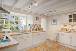 a kitchen with white cabinets and tile floors and windows at The Boy's Cottage in Portreath