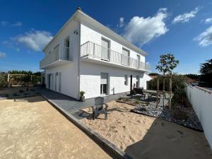 a white house with a balcony and a chair at 12 pers, sur la dune, PMR, spa, hammam, salle de sport in Barbâtre