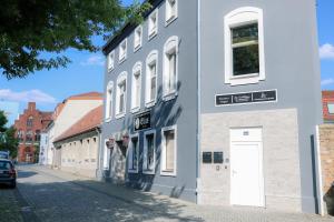a gray building with a white door on a street at Pension Hilges im Herzen der Altstadt in Schwedt