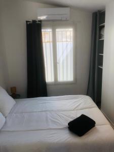 eine schwarze Tasche auf einem weißen Bett mit einem Fenster in der Unterkunft Maisonnette climatisée refaite à neuf avec parking à 300m de la plage in Le Grau-dʼAgde