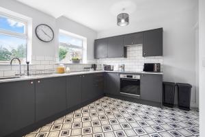 a kitchen with black cabinets and a clock on the wall at The Yorkshire Hosts - Central Castleford 4 Bed House - Free Parking in Castleford