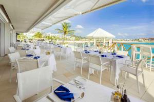 a restaurant with white tables and chairs and the ocean at Sonesta Maho Beach All Inclusive Resort Casino & Spa in Maho Reef