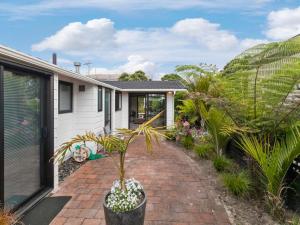 a house with a potted plant on a brick driveway at Sandy Toes Holiday Home Orewa in Orewa