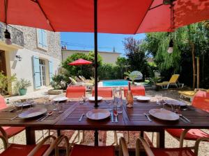 a wooden table with red umbrellas in front of a pool at La maison des Vendangeurs 10 in Olonzac