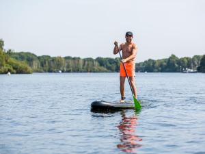 un homme debout sur une planche de paddle sur un lac dans l'établissement Beautiful chalet with air conditioning in a holiday park on the Leukermeer, à Well