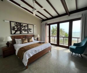 a bedroom with a bed and a chair and windows at Driftwood Villa in Pamunugama